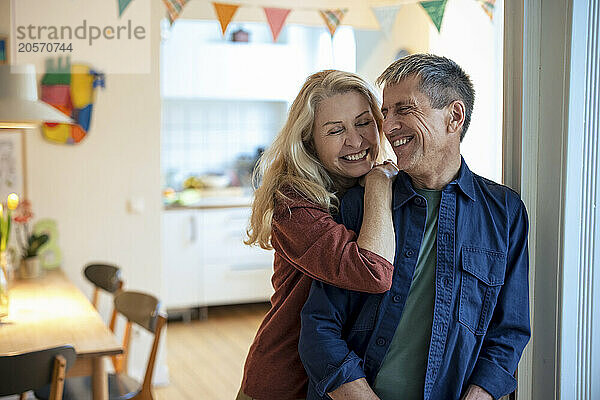 Happy senior woman leaning on man from behind at home