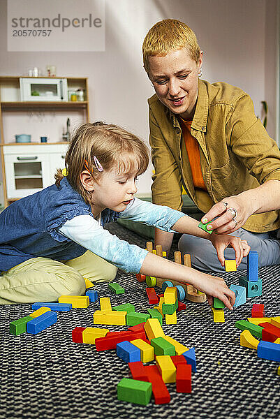 Mother and daughter playing with toy blocks sitting at home