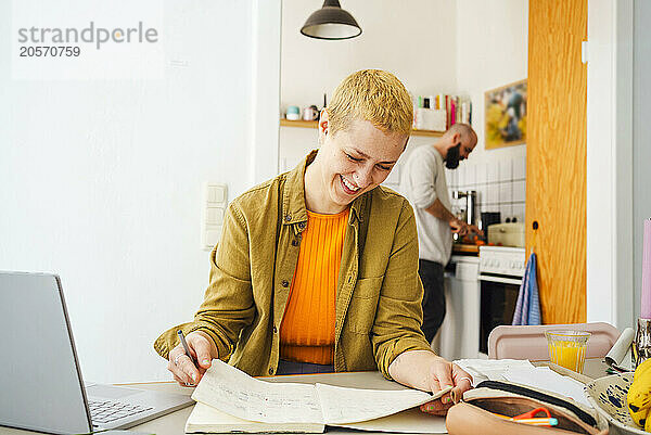 Smiling freelancer reading diary sitting at home office