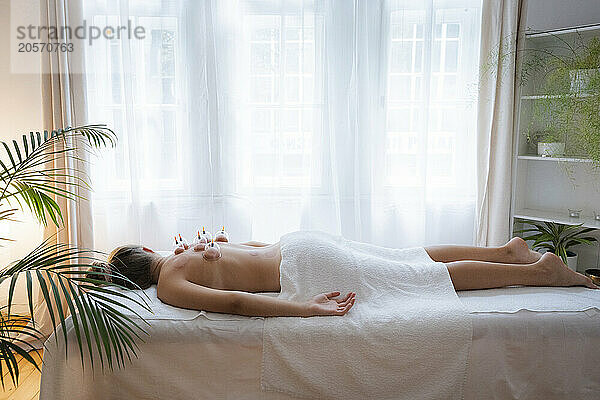 Teenage girl lying on front with vacuum cups on back in health spa