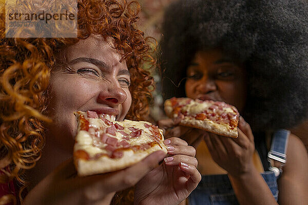 Multiracial roommates eating slice of pizza