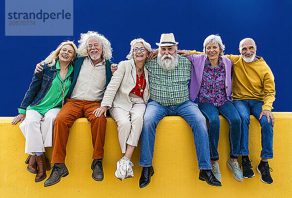 Carefree senior friends sitting on yellow wall