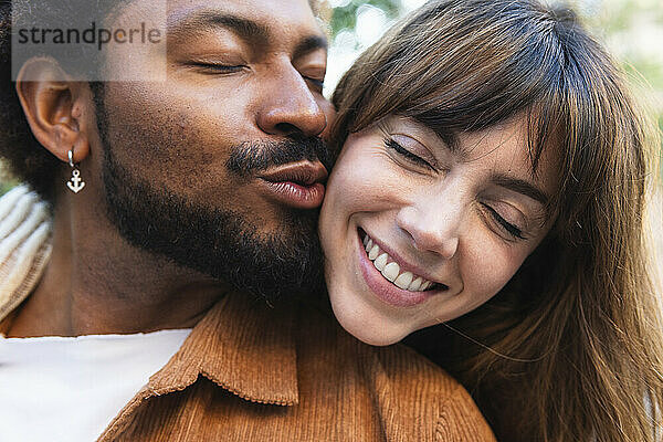 Man with eyes closed kissing girlfriend hugging from behind