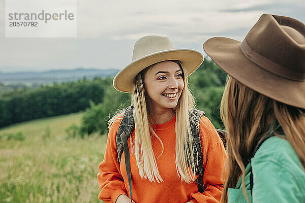 Smiling young woman wearing hat and discussing with friend on mountain