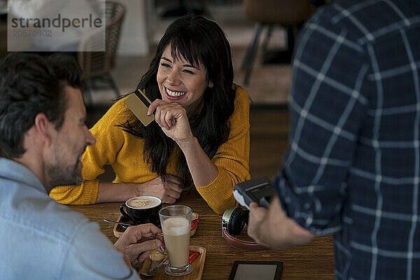 Happy businessman having coffee with colleague paying through credit card in cafe