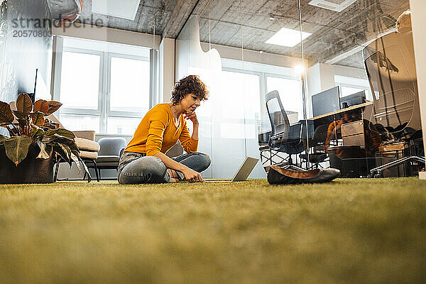 Businesswoman using laptop on carpet at office