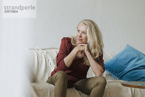 Smiling blond retired senior woman sitting on sofa in living room at home