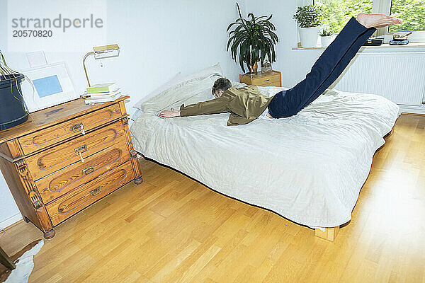 Young man jumping on bed at home