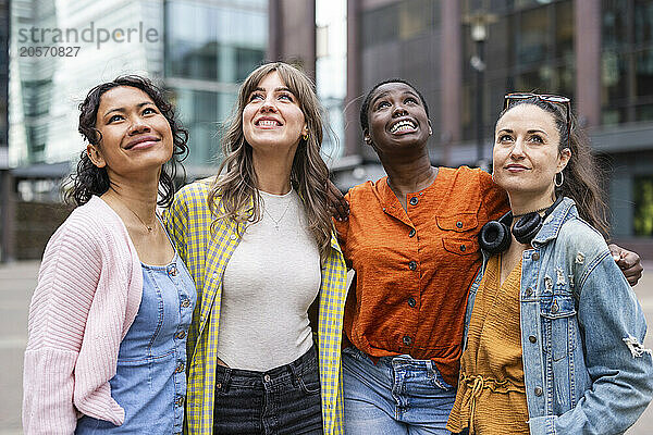 Smiling female friends looking up standing in city