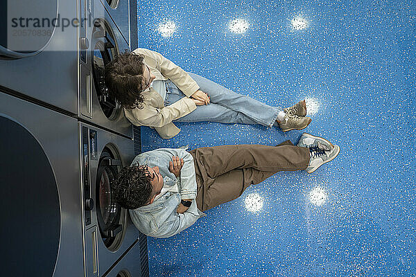 Young couple sitting together leaning on washing machines in laundromat