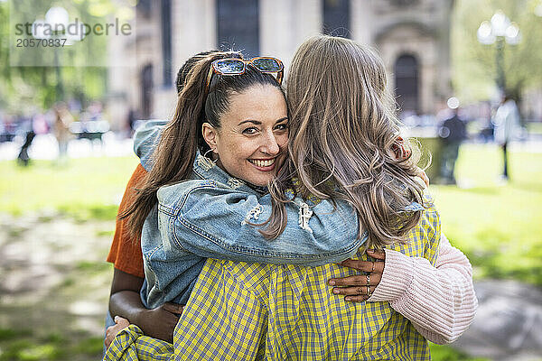 Smiling woman huddling with multiracial friends at park