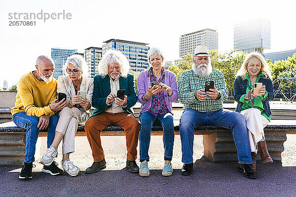 Friends using smart phones sitting together on bench