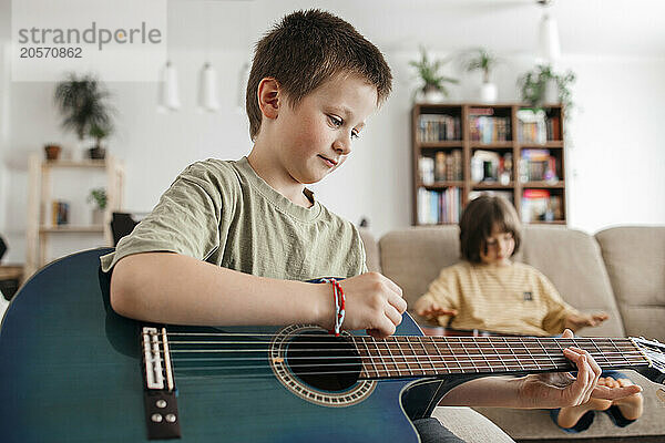 Cute boy trying to play guitar at home