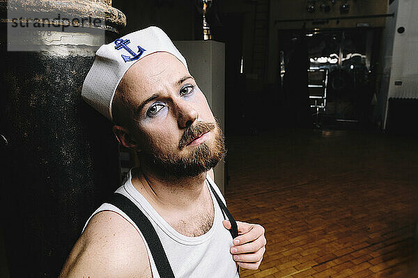 Gay man wearing sailor hat leaning on rusty column