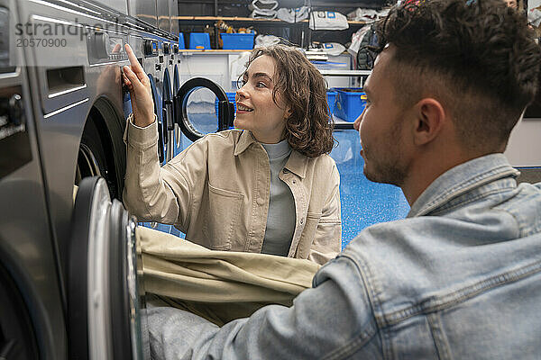 Young customers removing sheet from washing machine in laundromat