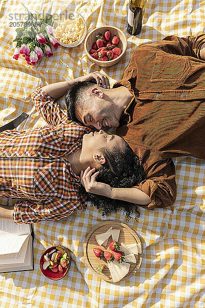 Happy young couple lying face to face on picnic blanket with each other