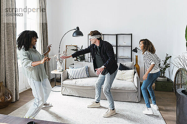 Happy parents playing blind man's buff with their daughter in the living room