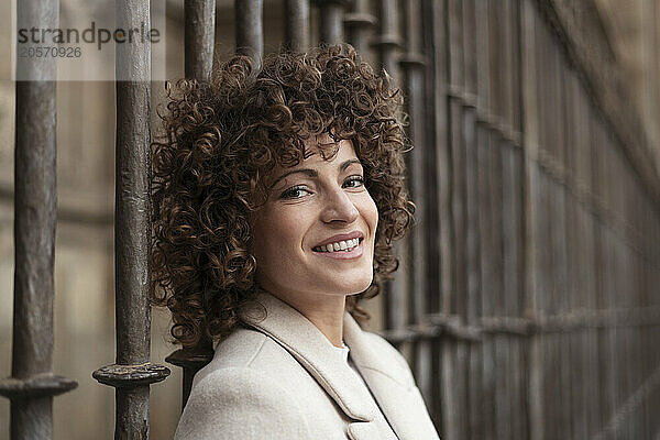 Smiling woman with curly hair leaning on metal fence