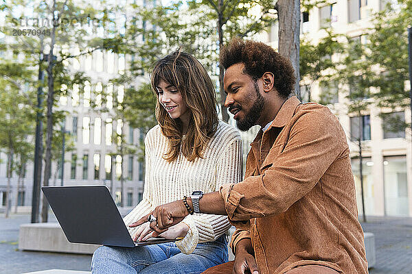 Smiling man pointing at laptop sitting with girlfriend