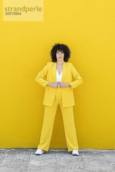 Confident woman wearing blazer standing on footpath in front of yellow wall