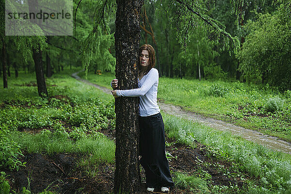 Young woman hugging tree in rain at forest