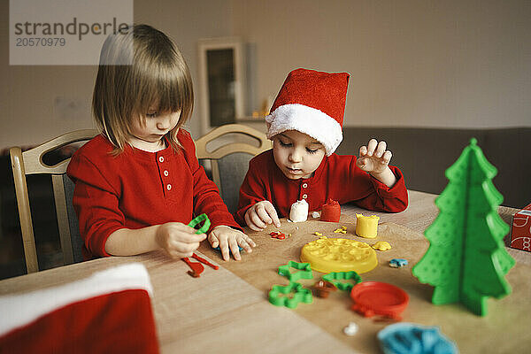 Siblings making plasticine Christmas tree decorations at home