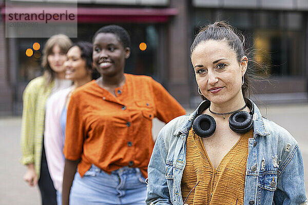 Smiling woman with wireless headphones standing in front of friends