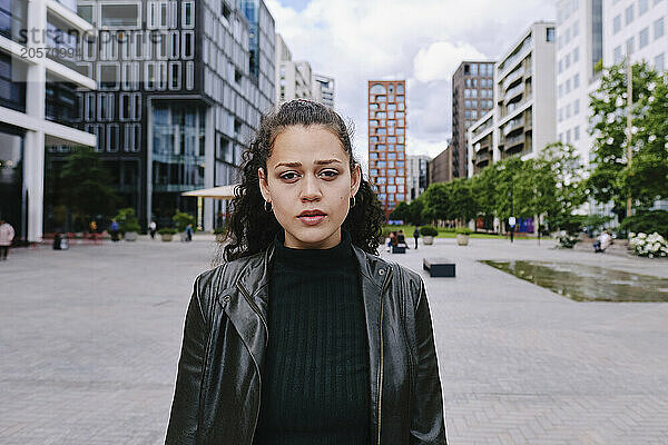 Beautiful young woman wearing black leather jacket standing in city