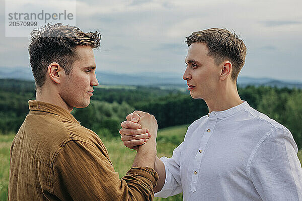 Confident young man holding hand and standing face to face at mountain