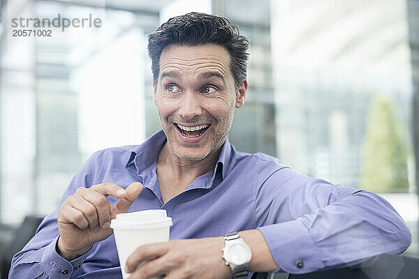 Cheerful mature businessman with disposable coffee cup sitting at airport terminal