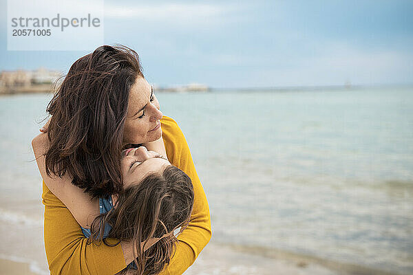 Girl embracing mother in front of sea at beach