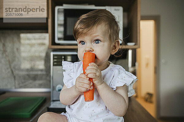 Cute girl eating carrot in kitchen at home