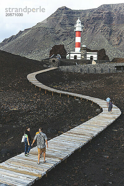 Friends walking on footpath leading towards Punta Teno Lighthouse in Spain