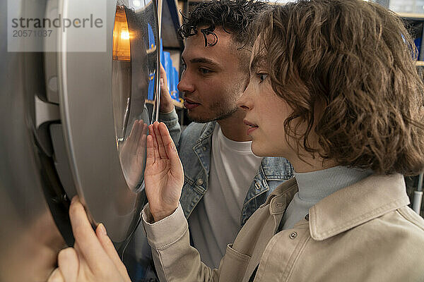 Couple looking inside washing machine at laundromat