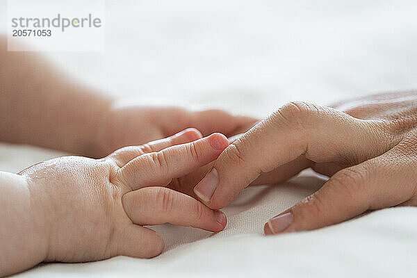 Hand of baby boy touching mother's finger on bed at home