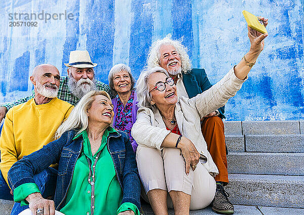 Happy woman taking selfie with friends sitting on steps