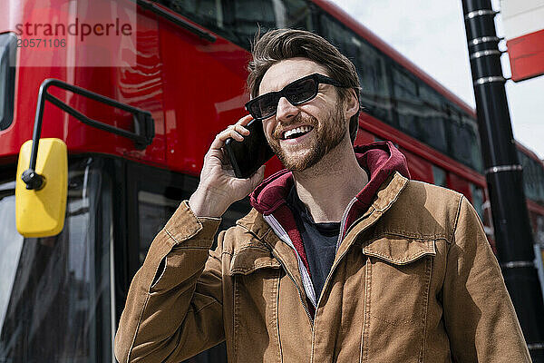 Happy man talking on smart phone near bus