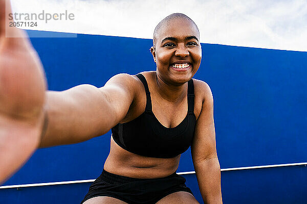 Happy bald woman taking selfie in front of blue wall