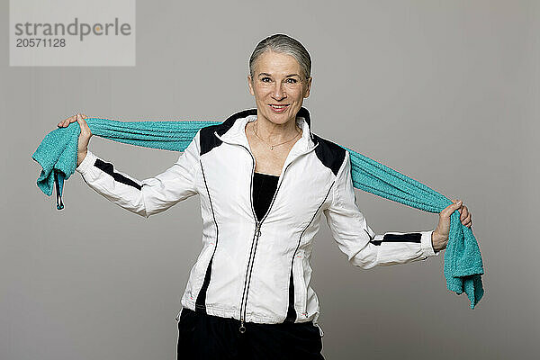 Smiling senior woman standing with turquoise towel against gray background