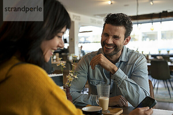 Happy mature businessman with businesswoman using smart phone in cafe