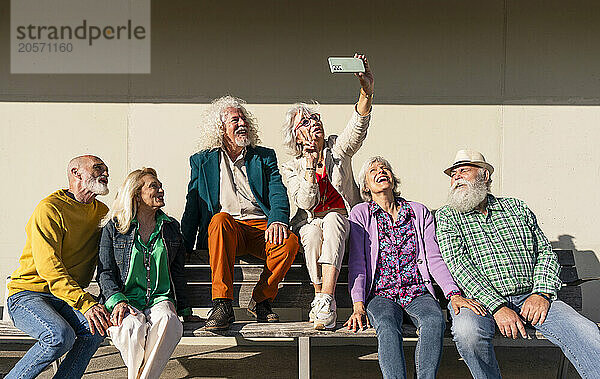 Happy woman taking selfie with friends sitting on bench