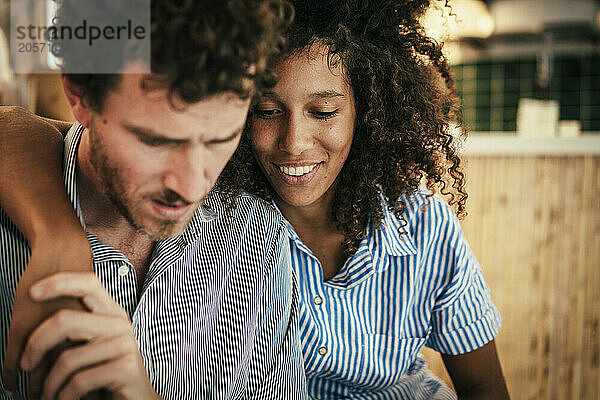 Smiling woman sitting with arm around boyfriend at cafe