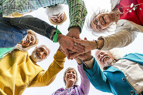 Cheerful elderly friends stacking hands together