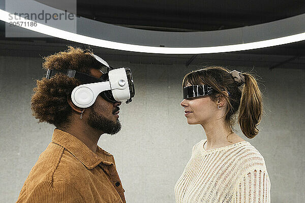 Multiracial couple wearing virtual reality simulators standing in front of each other