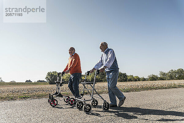 Friends holding mobility walker and walking at country road