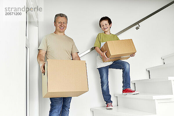 Happy father and son with cardboard boxes standing on staircase in new home