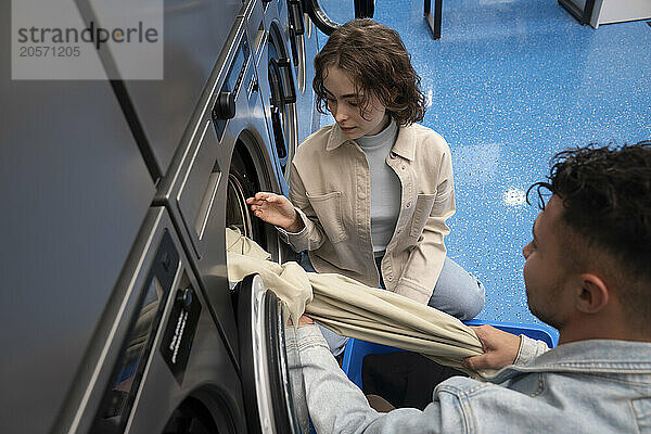 Young woman and man removing sheet from washing machine in laundromat