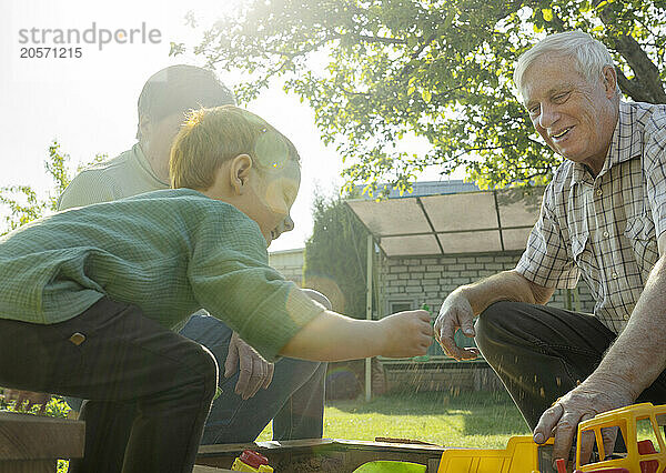 Happy grandfather and grandmother playing with grandson in back yard on sunny day