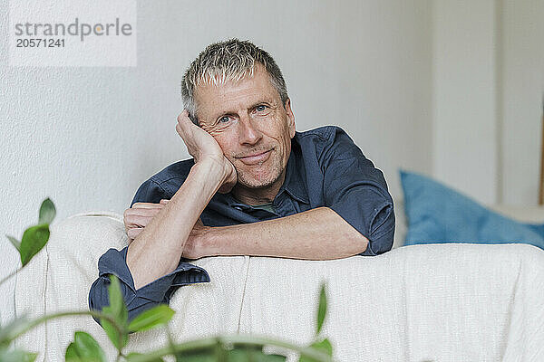 Smiling retired man leaning on sofa at home