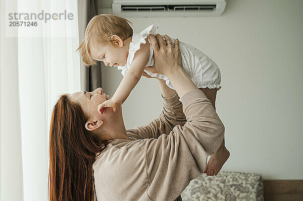 Happy redhead woman holding aloft daughter at home